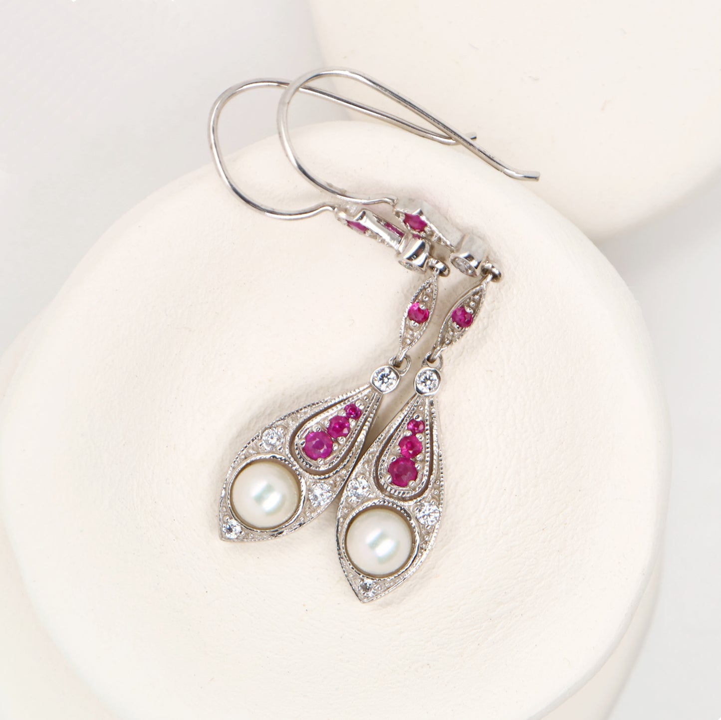 Silver earrings with pearls and red gemstones on a white background
