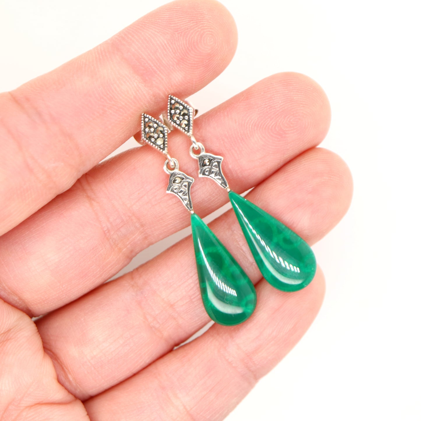 Green teardrop earrings with silver hooks held in a hand against a white background