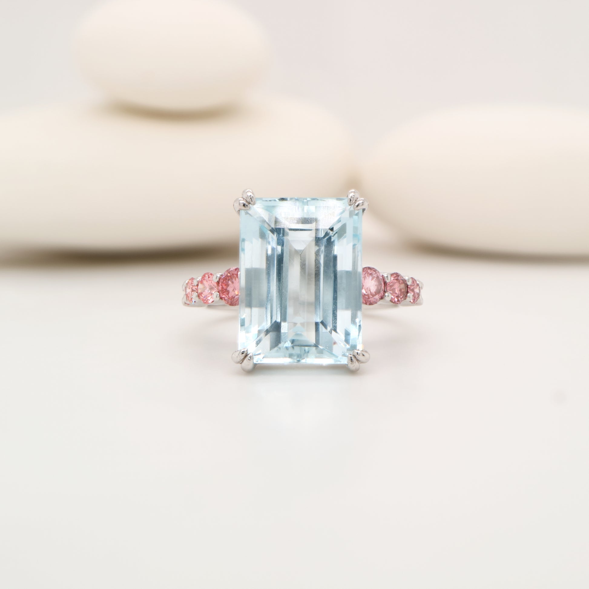 Ring with a large emerald-cut gemstone and smaller pink gemstones on a light background