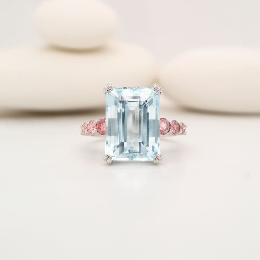 Ring with a large emerald-cut gemstone and smaller pink gemstones on a light background