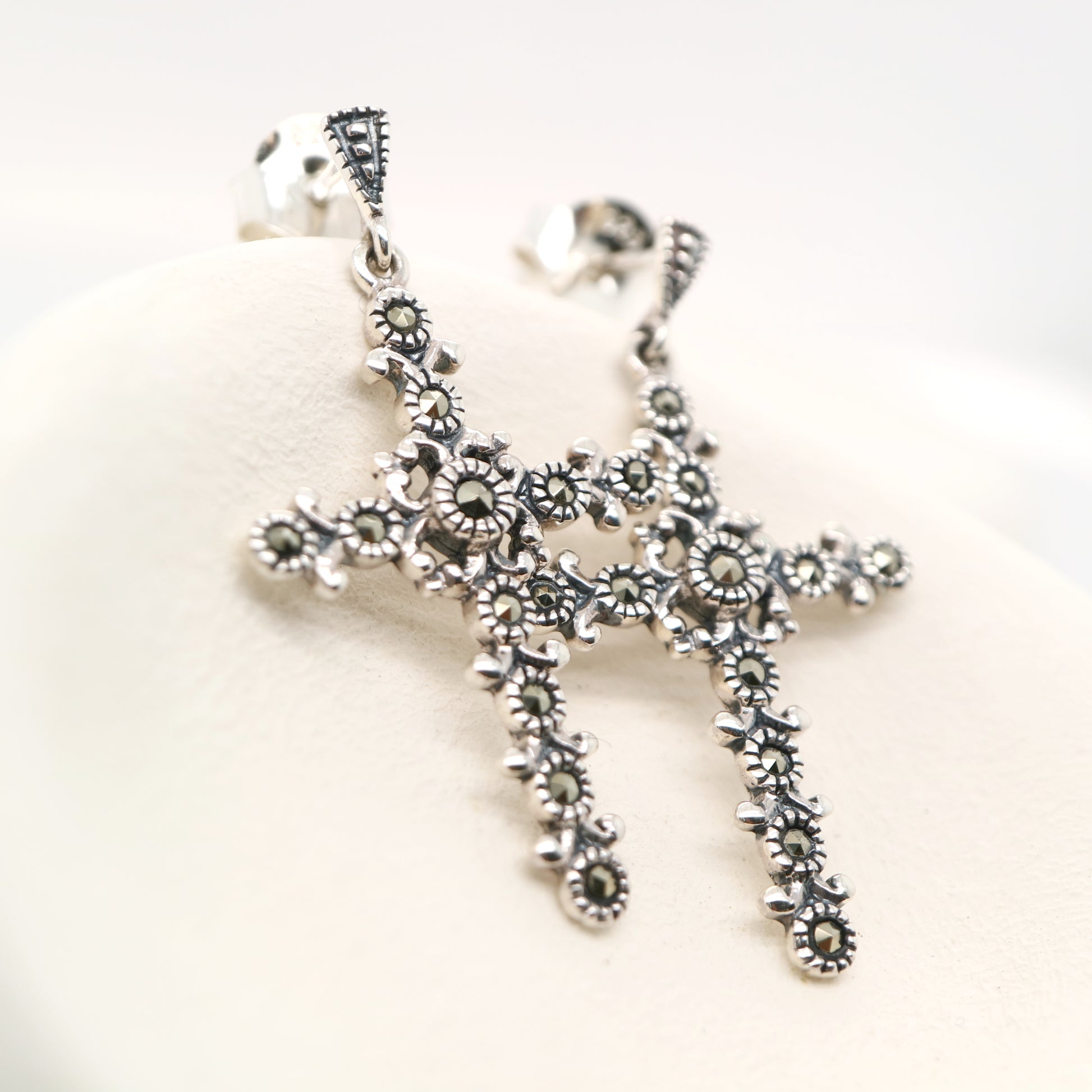 Silver cross pendant with floral designs on a white background
