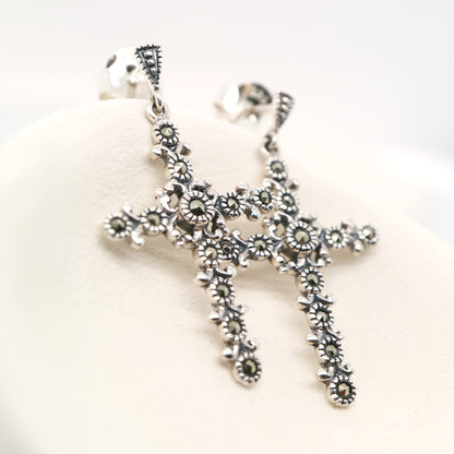 Silver cross pendant with floral designs on a white background