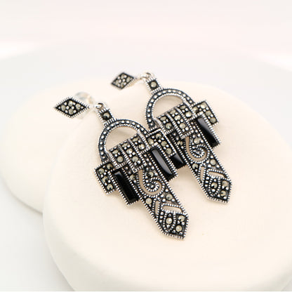 Pair of ornate black and silver earrings on a white background