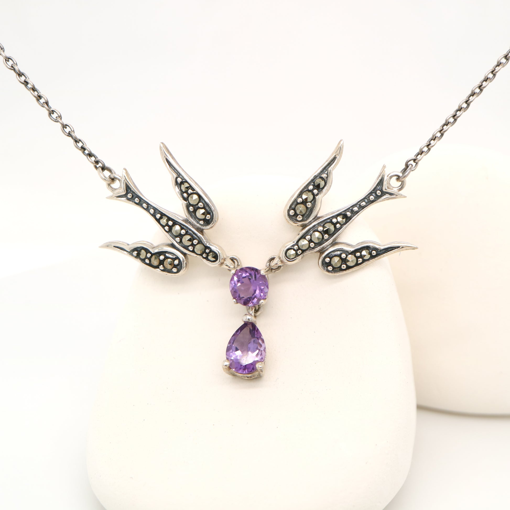 Necklace with bird-shaped design and purple gemstones on a white background