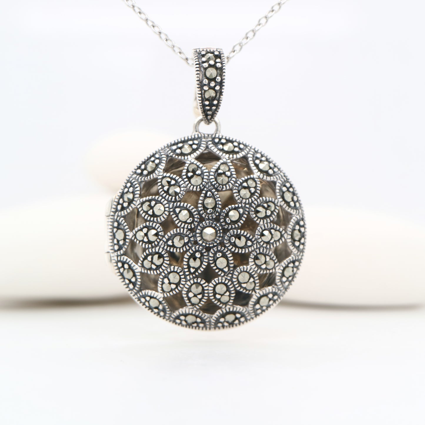 Silver necklace with a round, intricately designed pendant on a white background