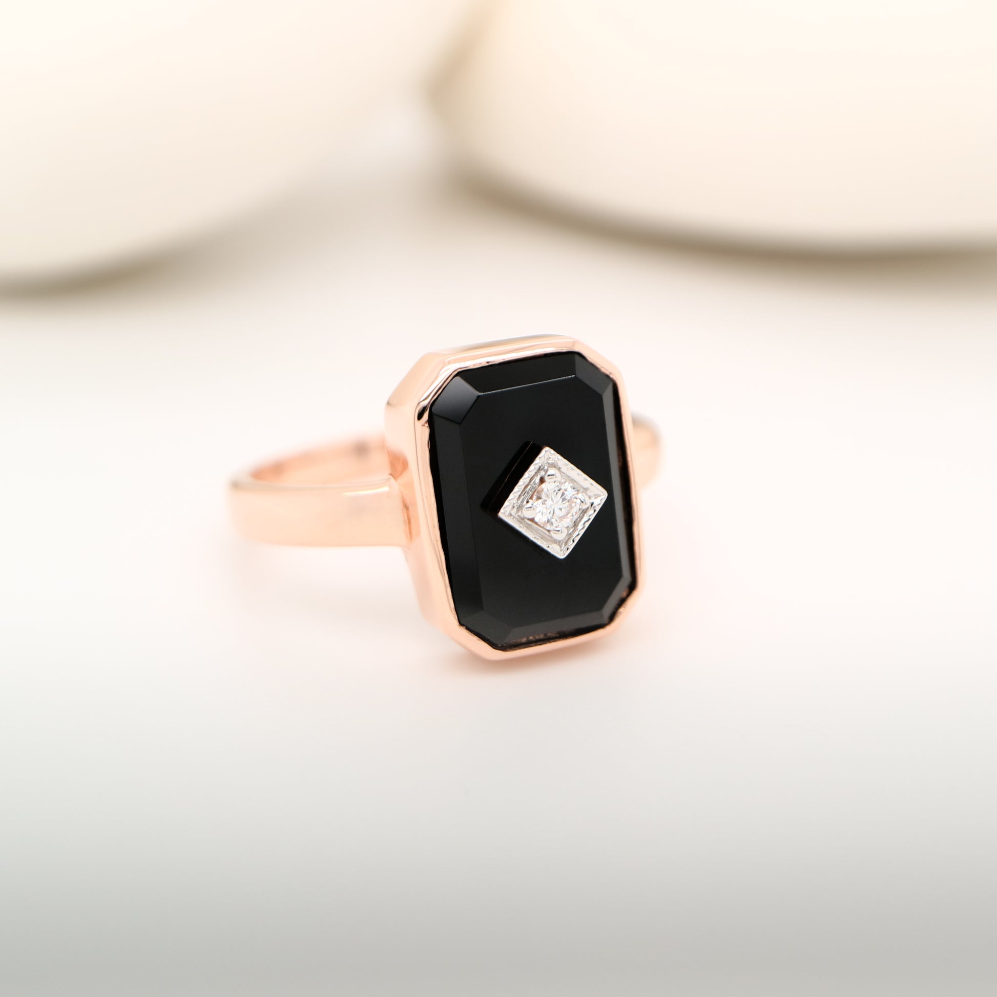 Rose gold ring with a black gemstone and smaller diamond on a light background