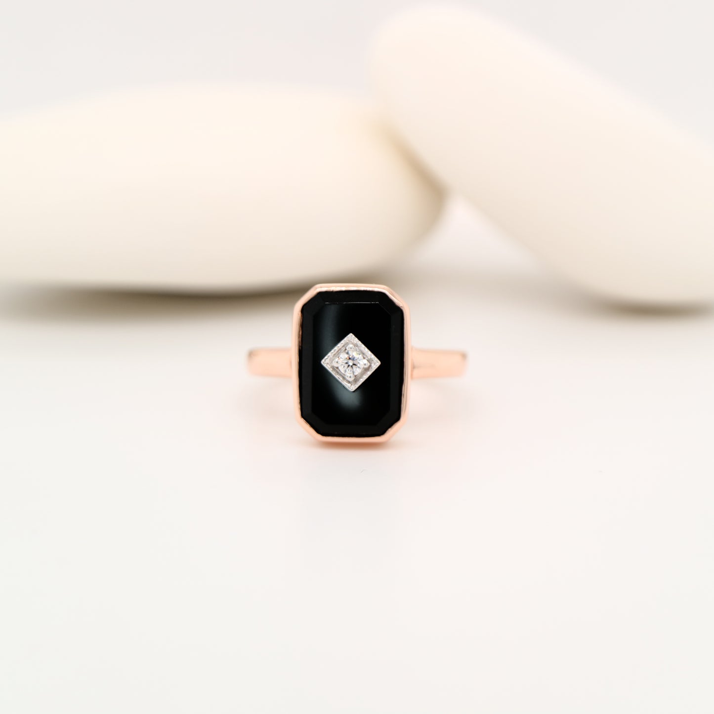 Rose gold ring with a black gemstone and diamond on a white background