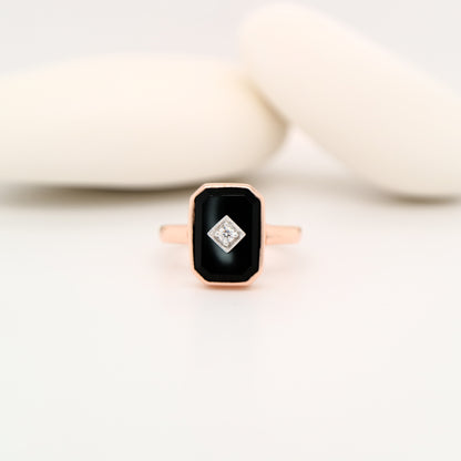 Rose gold ring with a black gemstone and diamond on a white background