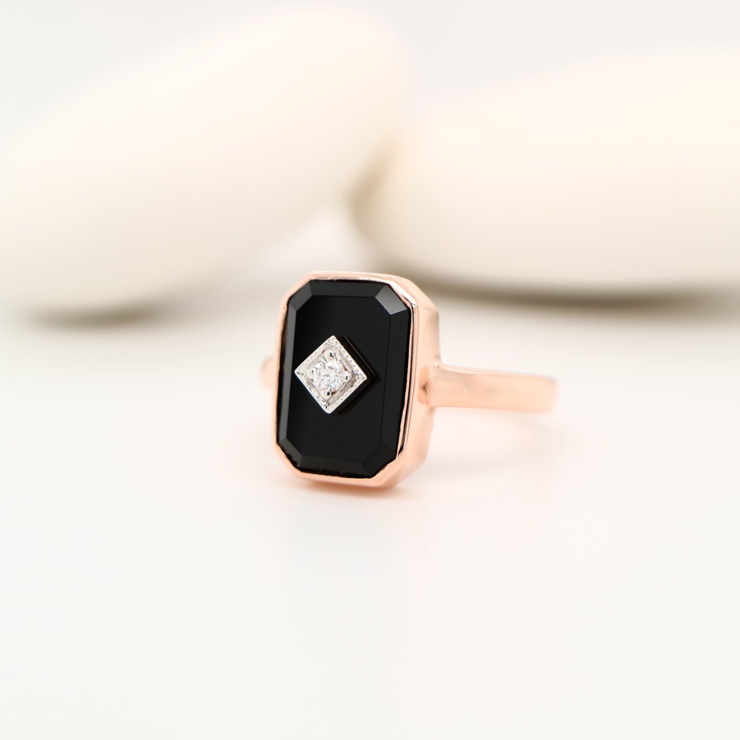 Rose gold ring with a black gemstone and smaller diamond on a light background