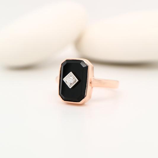 Rose gold ring with a black gemstone and smaller diamond on a light background