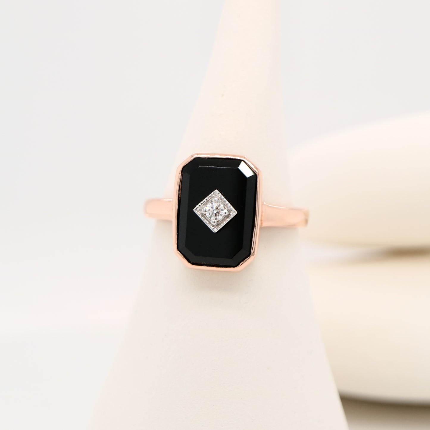 Rose gold ring with a black gemstone and diamond on a light background