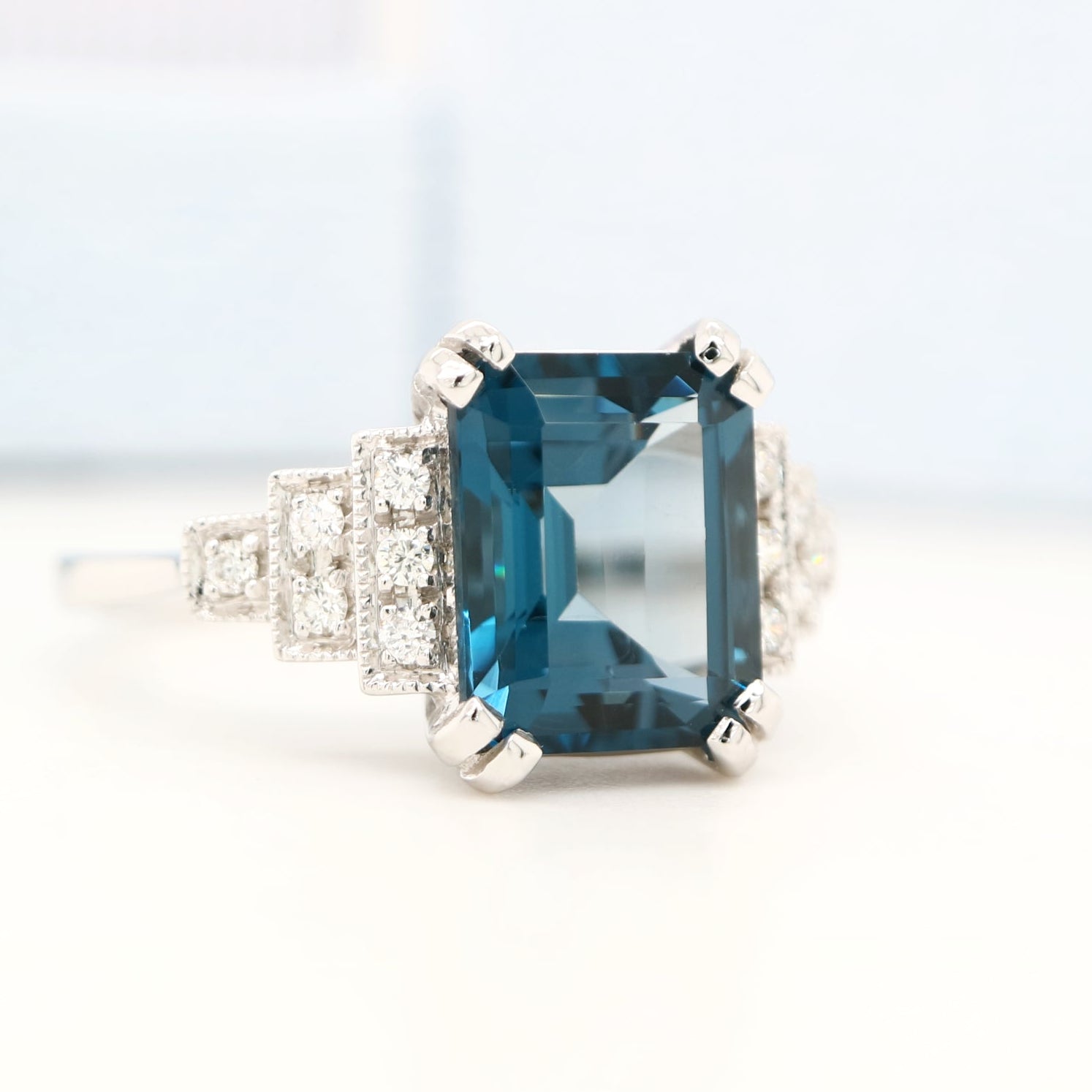 Ring with a blue gemstone and diamond-studded band on a light background